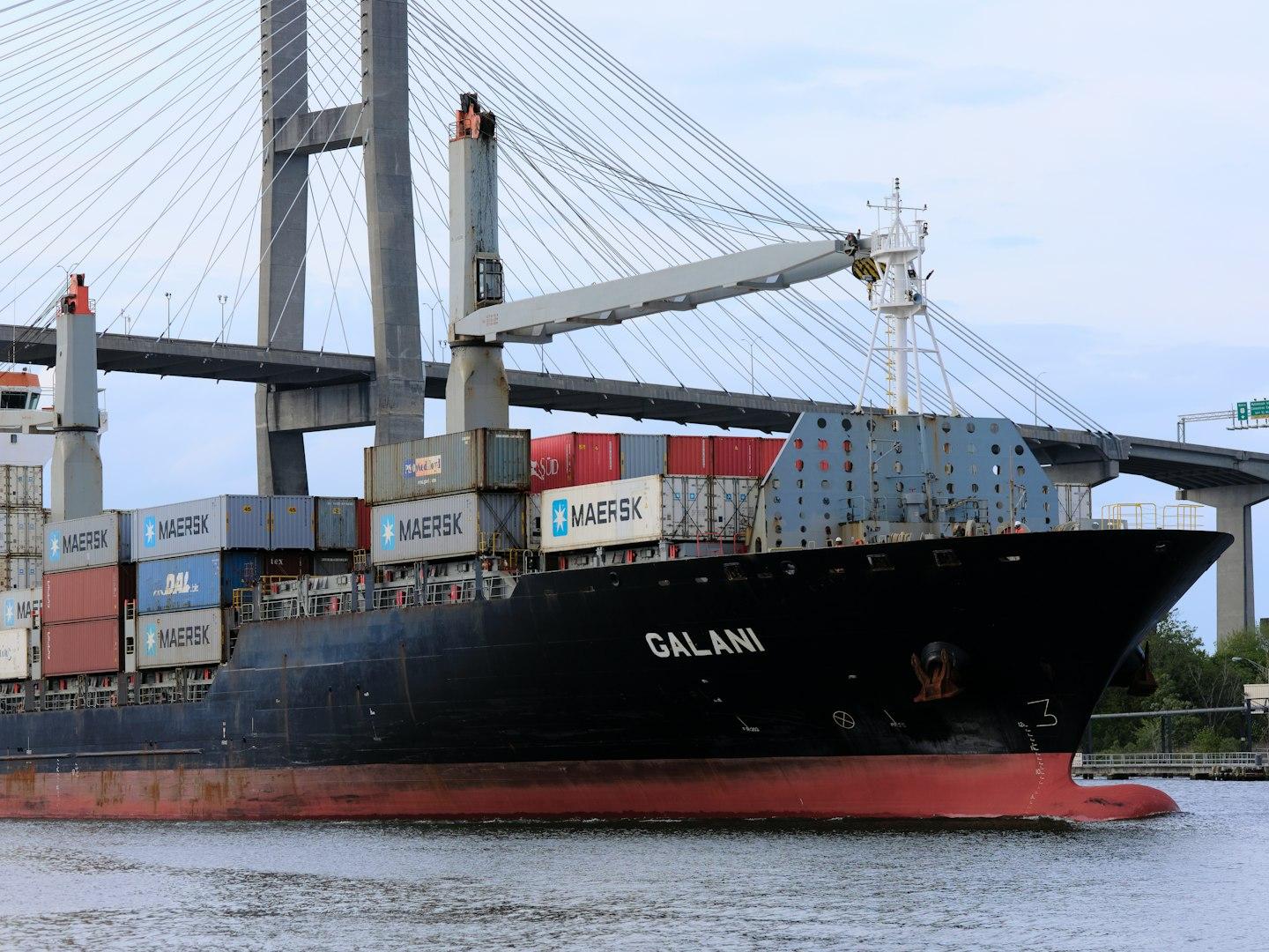 a large cargo ship in the water under a bridge